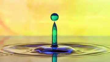 a liquid drop breaking the surface against a bright yellowish background